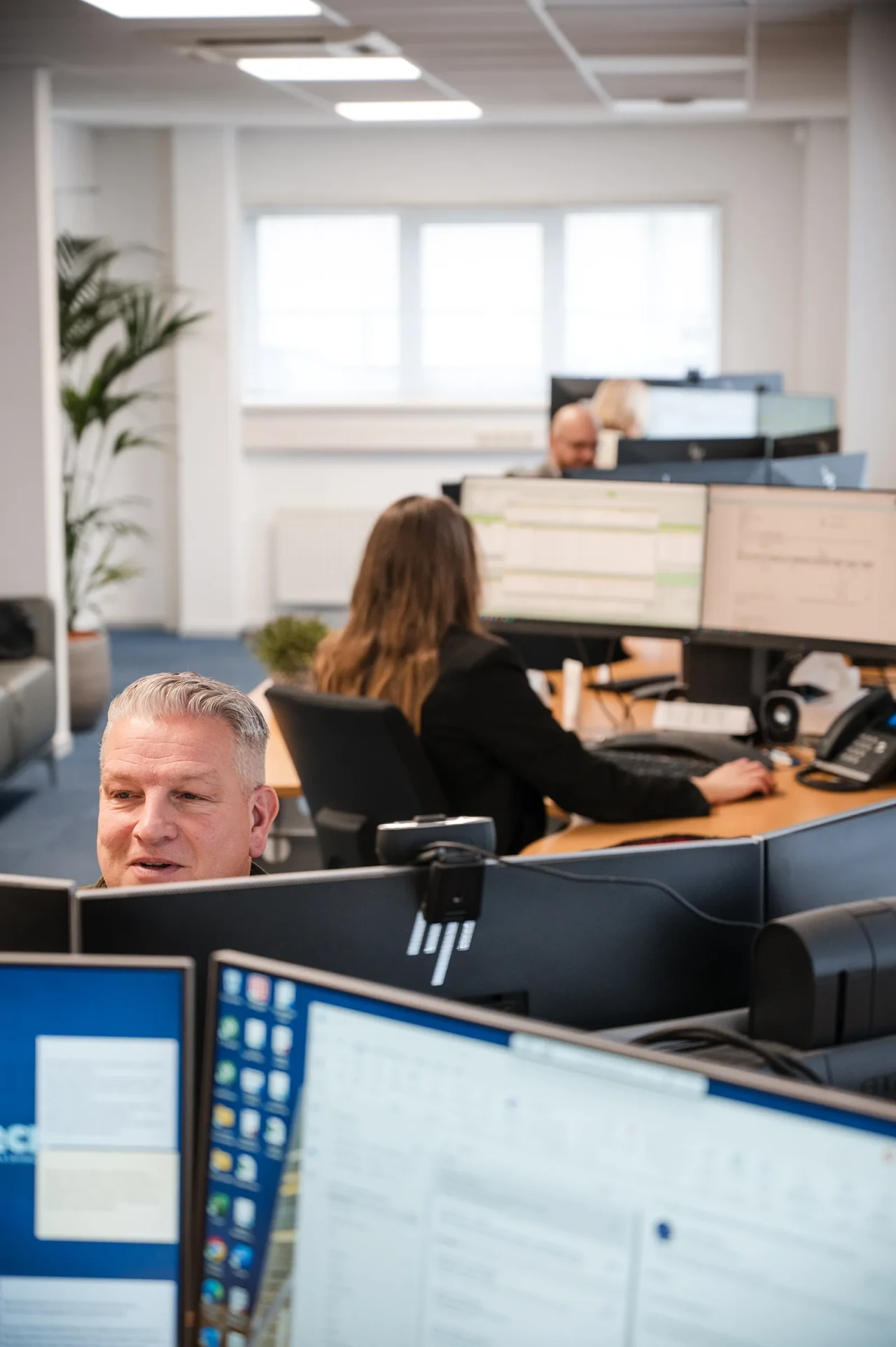 Imatech employees work at multiple computer stations in a bright office, focused on technical and customer support tasks.